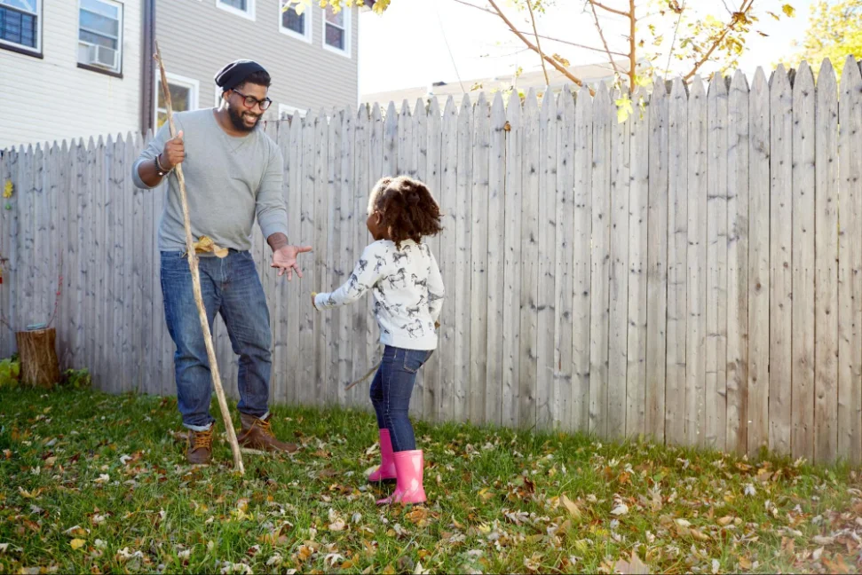 Father and daughter playing in garden stood next to solid wood fencing