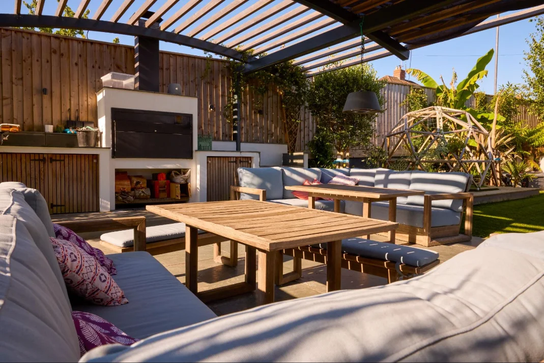 Outdoor room with a kitchen in the garden against sturdy fencing under shade from a pagoda